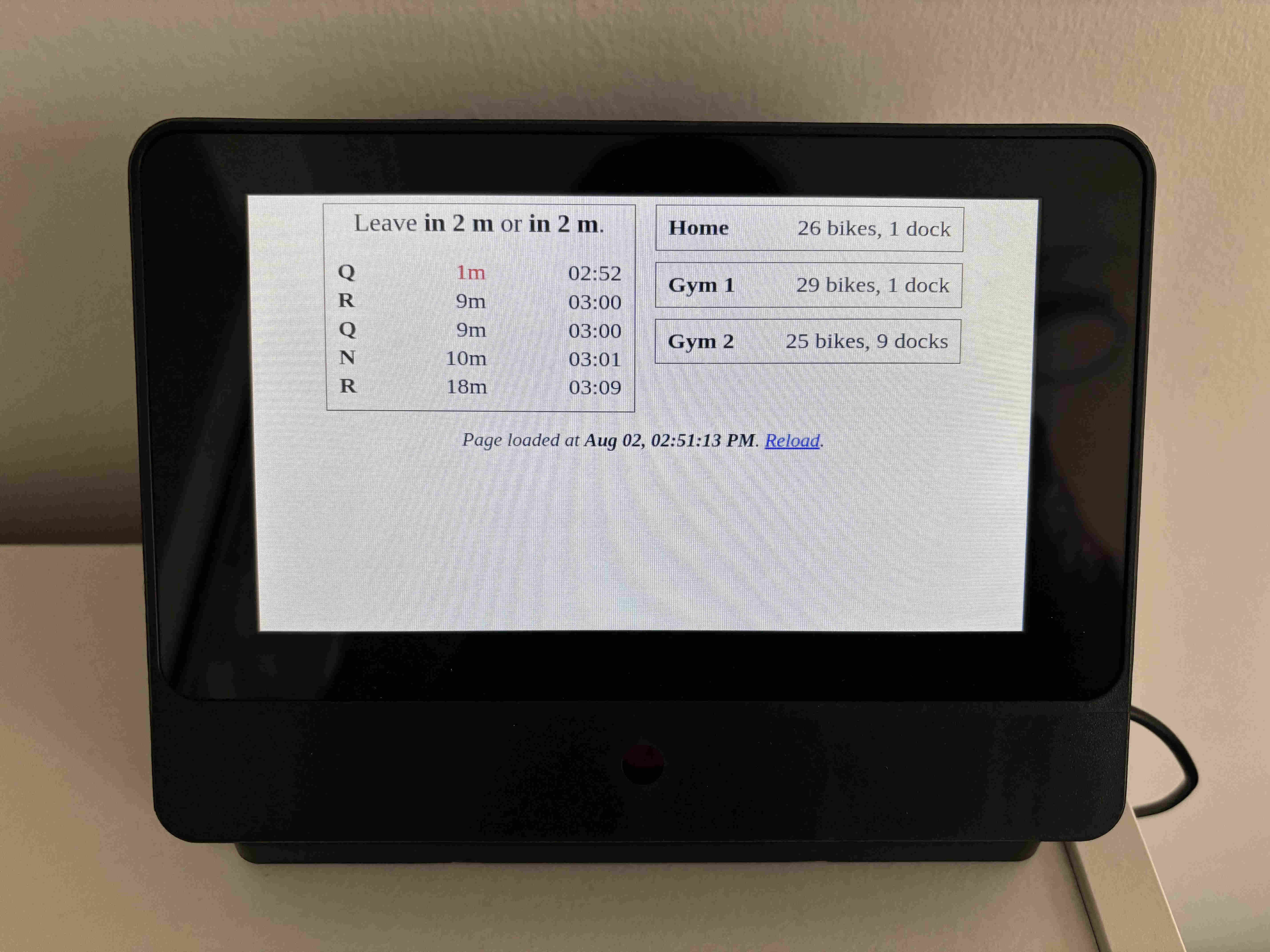 An electronic display atop a bookshelf, showing a listing of subway arrival times and bike stations with counts of bikes and docks